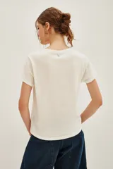 Remera de algodón blanca con cuello redondo y estampa frontal con el texto 'BLUE JEAN BABY' enmarcado en un recuadro negro.