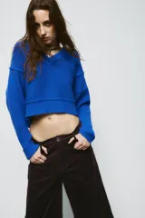Jersey de punto color azul eléctrico con escote en pico, manga larga y detalle de costuras marcadas en los hombros. Presenta un corte ligeramente cropped con puños y ruedo acanalados.