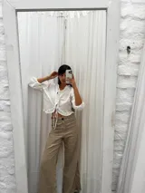 Blusa corta blanca de lino con mangas 3/4 abullonadas, escote en V con volados y cierre con lazos.