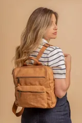 Mochila urbana de tamaño mediano confeccionada en símil cuero color crema. Presenta un diseño estructurado con asa superior, correas ajustables, un compartimento principal con cierre y un bolsillo frontal con cierre y detalle de costuras verticales.