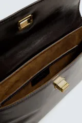 Bolso de mano tipo sobre color marrón oscuro, confeccionado en cuero. Cuenta con cierre de solapa con broche metálico dorado y asa de mano.