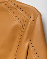 Campera estilo motero de símil cuero color habano, con cuello mao, cierre frontal, calce entallado y detalles de tachas en hombros y mangas.