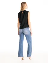 Blusa sin mangas color blanco, confeccionada en crepe con acabado satinado. Presenta un cuello alto decorado con mostacillas y una sobrecapa drapeada en el frente. La espalda cuenta con una abertura tipo gota y cierre de botón.
