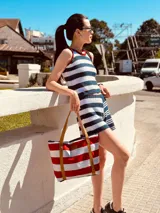 Bolso tipo tote rayado en rojo y blanco, con asas de cuero marrón.