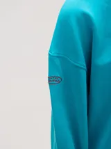 Buzo oversize color gris melange con corte crew, cuello redondo, mangas largas y detalles bordados en color verde en el cuello, puños y ruedo. Presenta el logo de la marca bordado en el pecho.