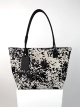 Cartera tipo tote confeccionada en cuero genuino con estampado animal print de vaca. Cuenta con cierre superior, correas de hombro fijas y un dije colgante de cuero con el logo de la marca.