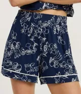 Pijama de dos piezas compuesto por una blusa de manga corta con cuello y cierre de botones, y un short con cintura elástica. El conjunto es de color azul marino con un estampado integral de flores y frutas en blanco, con ribetes blancos en los bordes.