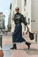 Bota de caña media confeccionada en cuero vacuno negro, con diseño minimalista y cierre trasero. Presenta un taco cilíndrico de madera tallada y punta cuadrada.