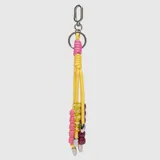 Llavero decorativo compuesto por cordones amarillos con nudos en color rosa, adornado con cuentas de plástico en tonos rosa, amarillo transparente con letras blancas y bordó, finalizado con terminales metálicos.