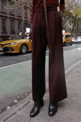 Pantalón de tiro alto color bordó, con pinzas delanteras, bolsillos frontales y falsos bolsillos con solapa en la espalda. Tiene pernera ancha y cierre frontal con cremallera, botón interior y gancho.