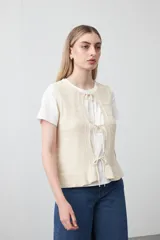 Chaleco tejido color verde musgo, con trama texturada, cuello a la base y cierre frontal con lazos. Presenta un ruedo con volado.