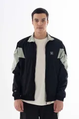 Campera negra de nylon con recortes en forma de V en color gris en las mangas. Tiene cuello mao, cierre frontal, puños y cintura elásticos, bolsillos laterales y logo estampado en el pecho y en la manga izquierda.