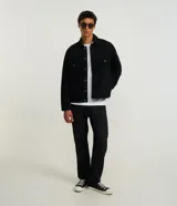 Campera trucker masculina de jeans negro, con cuello inglés, manga larga ajustada, cierre abotonado, bolsillos delanteros y sin estampa.
