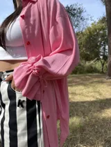 Camisa oversize de fibrana color rosa con botones rojos en forma de corazón y mangas largas con ajuste en los puños.