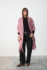 Chal de tejido de punto con textura acanalada, color rosa, con terminación de flecos en los extremos y etiqueta de cuero con logo de la marca.
