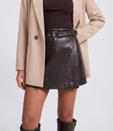 Short pollera corto de poliuretano color marrón oscuro, con diseño cruzado en el frente, cintura fija y cinturón incorporado con hebilla metálica.