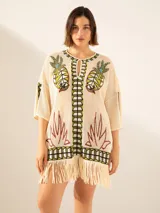 Poncho de hilo color crudo con diseño de ananás y motivos geométricos en tonos verde, marrón y negro. Posee flecos en el ruedo.