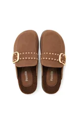 Pantuflas negras de gamuza sintética con interior de corderito, detalle de tira con tachas metálicas doradas y hebilla decorativa, y suela de corcho.