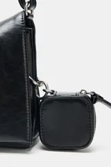 Bolso de hombro tipo baguette en color negro, con acabado brillante y estructura rectangular. Cuenta con una correa combinada de cadena metálica plateada y cuero sintético, y un pequeño monedero extraíble unido a un lateral. Presenta detalles de cordones decorativos en el otro lateral y cierre mediante solapa con imán.