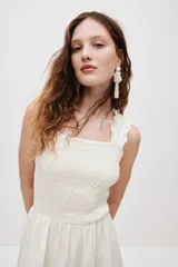 Vestido midi blanco de popelina de algodón, con cuerpo fruncido tipo nido de abeja, escote cuadrado y tirantes anchos con volantes que se cruzan en la espalda. Falda con ligero vuelo.