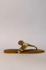 Sandalia plana de gamuza marrón, estilo ojota, con apliques metálicos dorados y hebilla decorativa.