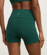 Bermuda deportiva de alta compresión Get Over, color verde oscuro, de tiro alto con cintura doblada y detalle de bies blanco contrastante en el lateral.