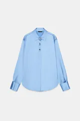 Camisa de cuello solapa y manga larga, confeccionada en tejido satinado con acabado brillante. Presenta cierre frontal con botones y bajo asimétrico.