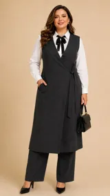 Chaleco largo de corte sastrero en color gris oscuro con sutil estampado de rayas verticales. Presenta un diseño cruzado con cierre de lazo lateral, escote en V profundo y bolsillos laterales funcionales.