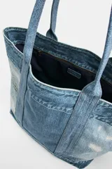 Bolso tipo shopper de hombro efecto denim, confeccionado con paneles de mezclilla de diferentes lavados y detalles deshilachados. Cuenta con doble asa de hombro y bolsillo interior con cremallera.