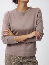 Buzo de punto fino color marrón topo, con cuello redondo y detalle de botones decorativos dorados sobre el hombro izquierdo. Presenta mangas largas con puños acanalados y una pequeña abertura lateral en los mismos.