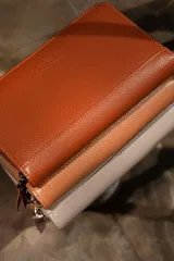 Billetera de cuero color marrón, con cierre de cremallera y múltiples compartimentos para tarjetas, billetes y monedas.