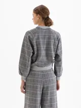Buzo tipo bomber de tela de punto con estampado de cuadros, cuello redondo, puños y ruedo tejidos en color gris. Presenta cierre frontal con broches a presión y mangas largas con diseño holgado.