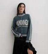 Campera tejida de algodón en color rojo, con cierre frontal completo, cuello alto y puños acanalados con detalles de rayas blancas. Presenta un diseño gráfico con texto blanco en el frente.