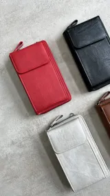 Cartera portacelular con correa larga, cierre con cremallera y solapa con broche imantado.