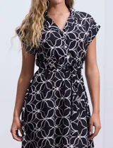 Vestido corto estampado en blanco y negro, marca Luxology. Escote en V cruzado con solapa, manga corta y falda acampanada. Cintura elastizada con pasadores y lazo de ajuste.