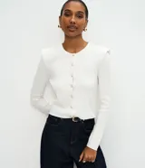 Cardigan de punto color blanco, de corte regular y ajuste al cuerpo. Presenta cuello redondo, mangas largas, cierre frontal con botones delicados y hombreras estructuradas que aportan volumen a la silueta.
