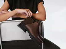 Botinetas negras con suela track, combinando cuero texturizado en la parte frontal y cuero charolado en la parte trasera. Diseño de caña baja con detalle de corte lateral.
