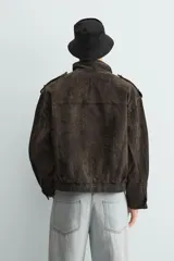 Cazadora de corte relajado confeccionada en piel con acabado de ante. Presenta cuello subido, cierre frontal de cremallera oculta por solapa con botones a presión, bolsillos de plastrón con solapa en el pecho y bolsillos de vivo en la cadera. Incluye trabillas en los hombros, mangas largas con puños abotonados y bajo con elástico.