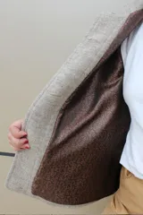 Campera de paño de lana en color beige jaspeado, con diseño oversize. Presenta detalles en pana color marrón chocolate en los puños y en las tapas de los bolsillos frontales. Cuenta con cierre frontal de botones grandes y cuello alto.