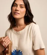 Vestido corto de viscolino color marfil con escote redondo, mangas cortas y bolsillos laterales. Cuenta con un estampado frontal en tonos de azul que representa un paisaje de palmeras y olas del mar.