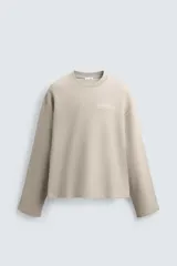 Sudadera de corte boxy fit confeccionada en tejido de mezcla de algodón, con cuello redondo y mangas largas. Presenta un diseño minimalista con texto estampado a contraste en el pecho y efecto lavado.