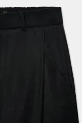 Pantalón negro de tiro alto y pernera ancha, confeccionado en tejido fluido, con bolsillos laterales y detalles de pliegues en la parte delantera.