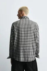 Camisa de corte relajado confeccionada en tejido fluido con estampado de cuadros. Presenta cuello solapa, cierre frontal de botones, manga larga con puños abotonados y una corbata integrada del mismo tejido.