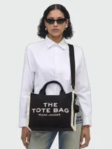 Cartera tipo tote bag Marc Jacobs modelo The Medium Tote, color negro con detalles en blanco, con asas de mano y correa de hombro ajustable y extraíble.