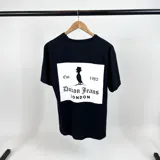 Remera negra de corte amplio con estampado blanco en el frente que incluye el logo de la marca Duxon Jeans, la silueta de un hombre con sombrero y el texto "Est. 1982 LONDON".