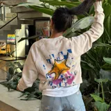 Buzo de cuello redondo color crudo, con diseño estampado en la espalda que presenta una estrella de mar estilizada sobre un fondo de formas geométricas abstractas en tonos azul, amarillo y rosa.