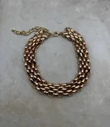 Collar de eslabones anchos y gruesos, de color dorado, compuesto por varias filas unidas que forman una estructura tipo malla o gargantilla ancha. Posee un cierre de mosquetón y cadena de ajuste.