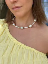 Collar corto de perlas de río alargadas y ovaladas, con cuentas de acero quirúrgico y bolitas con baño de oro. Cierre con cadena de acero quirúrgico y gancho para regular el largo.