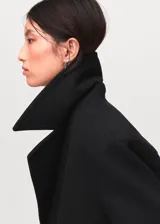 Abrigo de paño negro con diseño cruzado, cierre frontal de botones, cuello de solapa con muesca y mangas largas con puños abotonados.