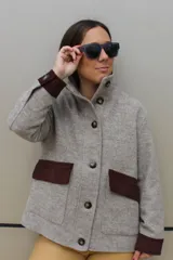 Campera de paño de lana en color beige jaspeado, con diseño oversize. Presenta detalles en pana color marrón chocolate en los puños y en las tapas de los bolsillos frontales. Cuenta con cierre frontal de botones grandes y cuello alto.